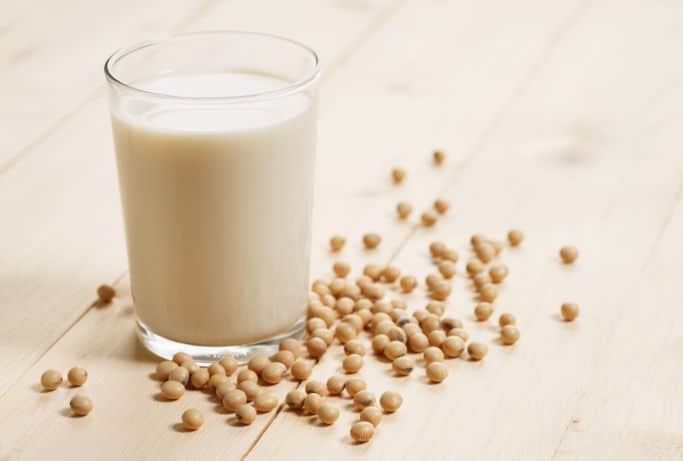 soy milk in glass surrounded by soy beans