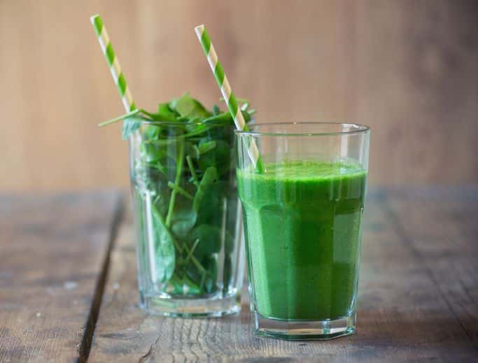 glass of spinach smoothie with glass of spinach leaves