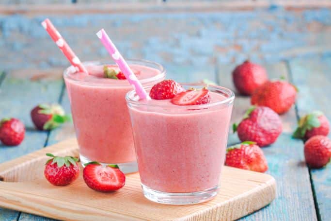 two strawberry smoothies on wooden cutting board