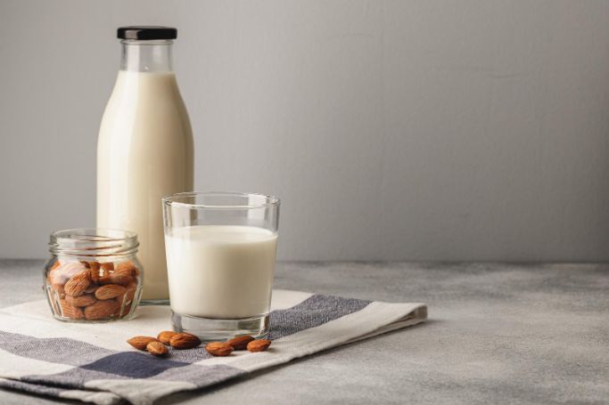 almond milk in glass and bottle with nuts on the side