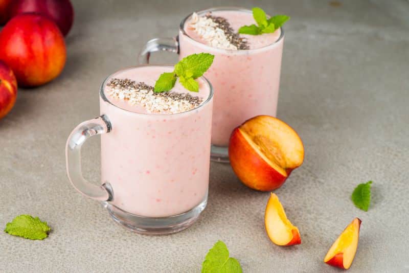 two peach strawberry smoothies with fresh peaches gray background