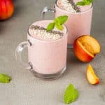 two strawberry peach smoothies with fresh peach beside the glasses